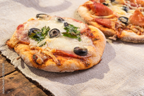 Traditional Italian appetizer - mini pizza, pizzetta with sausage, olives and mozzarella cheese on a linen napkin close-up - Neapolitan style