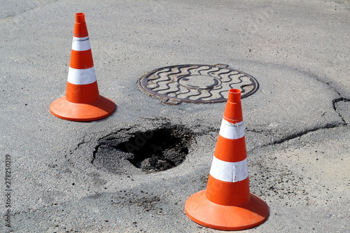 Pit in asphalt fenced with two signal cones. Safety movement.