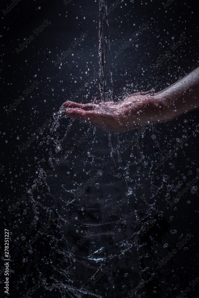 A Stream of Water Pouring Down a Caucasian Man's Hands - Splashing Droplets of Water Everywhere with a Black Background