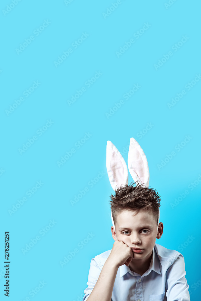 bored boy in a light shirt and Bunny ears on a blue background