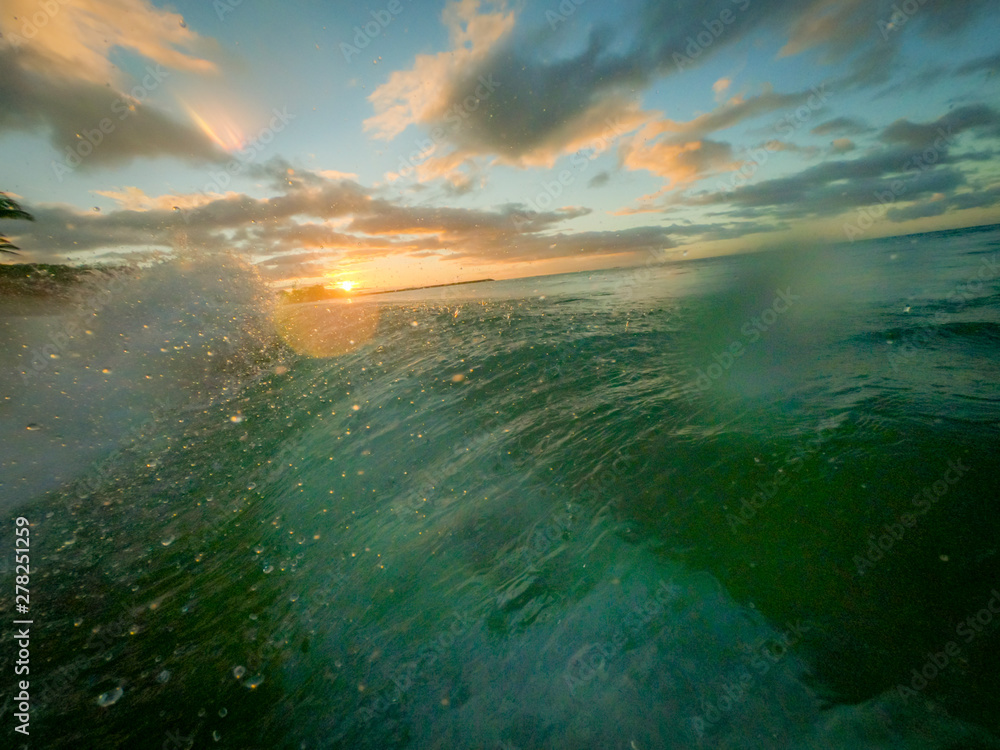 Fototapeta Zbliżenie fal rozbijających się o plażę w Oahu na Hawajach o zachodzie słońca - z czystą, wodną wodą i żywymi chmurami w tle