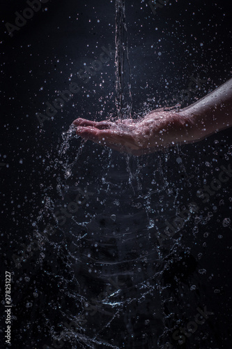 A Stream of Water Pouring Down a Caucasian Man's Hands - Splashing Droplets of Water Everywhere with a Black Background © Jon