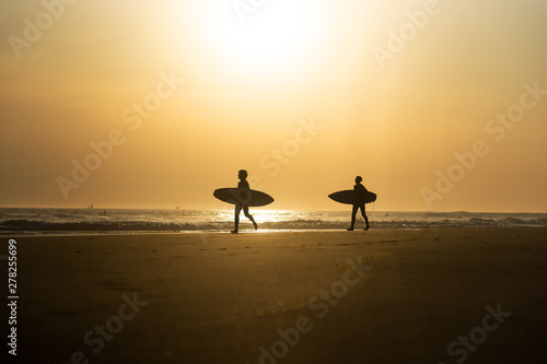 Silhouette of two young men with surf boards on beach at sunset,