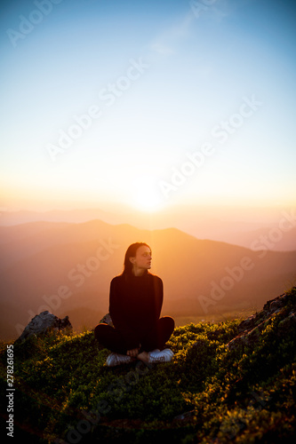Woman sitting on a rock over mountains at sunset. Girl on the background of mountain peaks. Woman hiking in mountains © Serhii