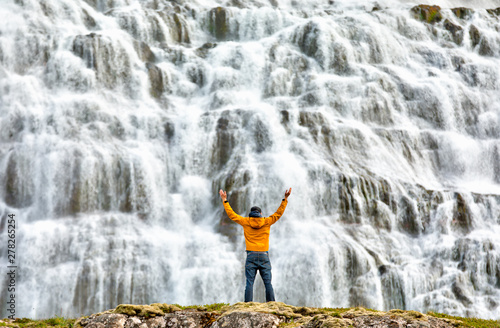 Fotografie, Tablou Man standing by beautiful cascades of famlus Dynjandi waterfall, Westfjords, Ice