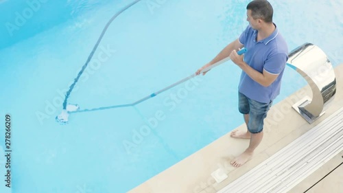 Man cleaning swimming pool with vacuum tube cleaner early in the morning.