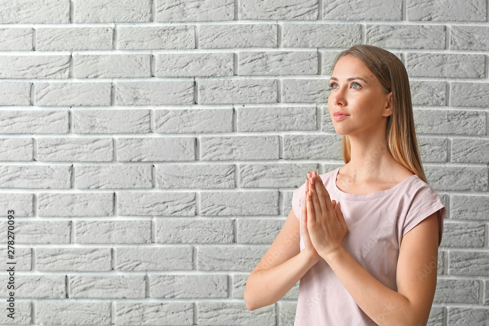 Religious young woman praying against brick wall