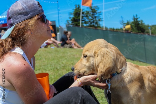 Casual Woman sitting on grass at music festival with her golden retriever puppy, bokeh effect