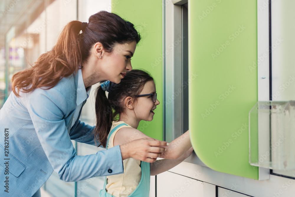 Young mother elegantly dressed with her daughter using ATM machine on city street. Young mother elegantly dressed with her daughter using ATM machine on city street.