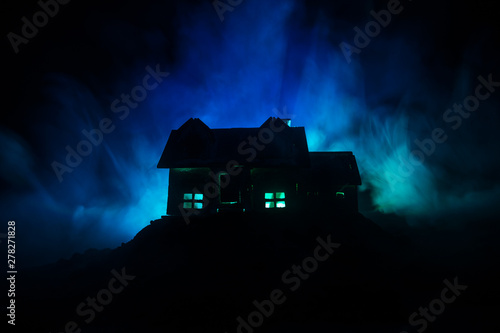 Old house with a Ghost in the forest at night or Abandoned Haunted Horror House in fog. Old mystic building in dead tree forest. Trees at night with moon. Surreal lights.