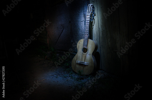 An wooden acoustic guitar is against a grunge textured wall. The room is dark with a spotlight for your copyspace.