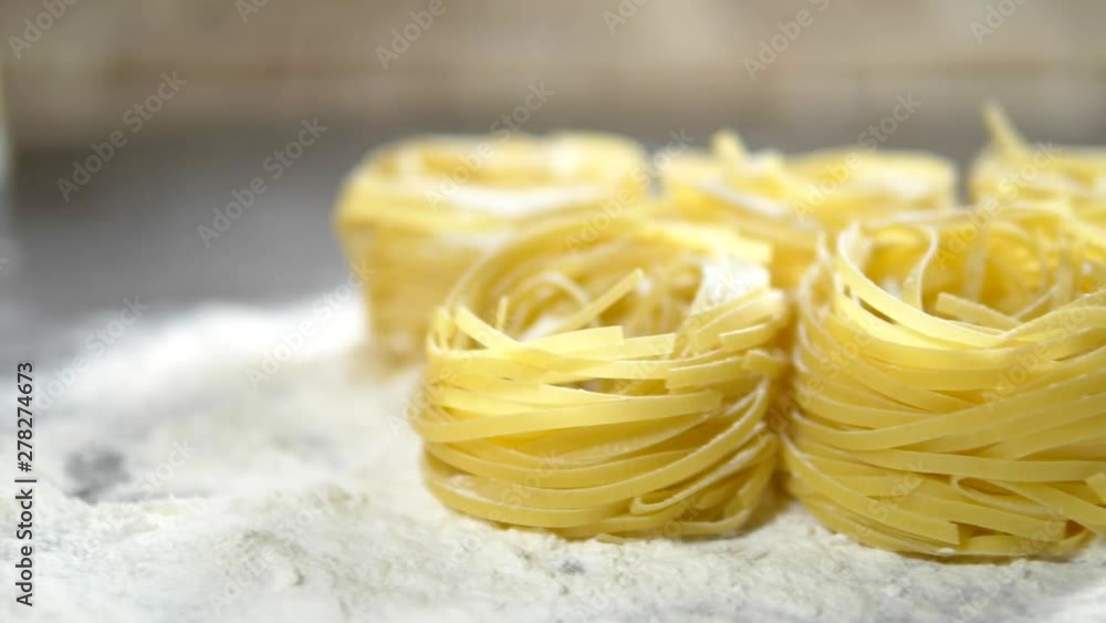 Fettuccine, raw pasta, closeup lie in white flour on a wooden table Fettuccine, raw pasta, closeup lie in white flour on a wooden table