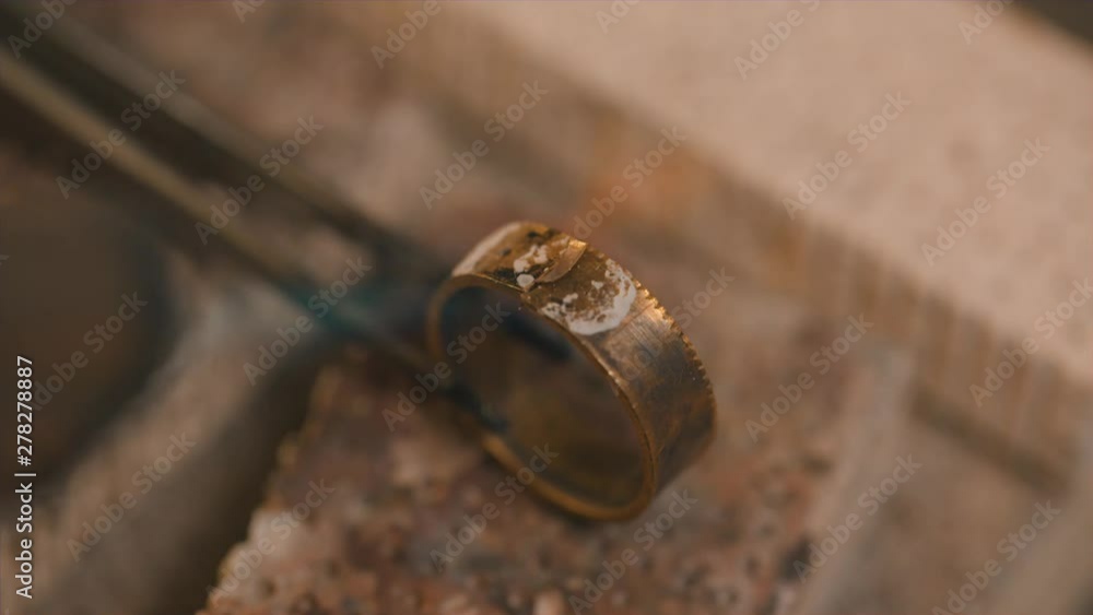 hand of a goldsmith holds a golden ring with tweezers in a gas flame to glow it, copy space in the dark background, selected focus, narrow depth of field hand of a goldsmith holds a golden ring with tweezers in a gas flame to glow it, copy space in the dark background, selected focus, narrow depth of field
