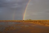 Tiny Figure at the End of a Rainbow in a Sunlit Outback Landscape