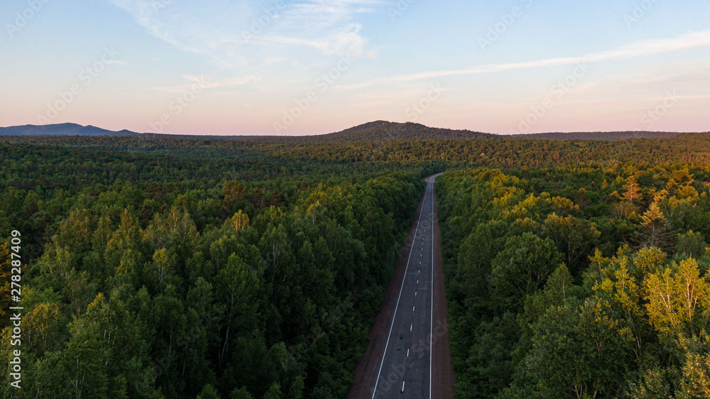 Top view of the dirt road and green spring forests in bright sunset colors. Beautiful landscape from the air, photograph from the drone.