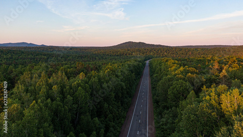Top view of the dirt road and green spring forests in bright sunset colors. Beautiful landscape from the air, photograph from the drone.