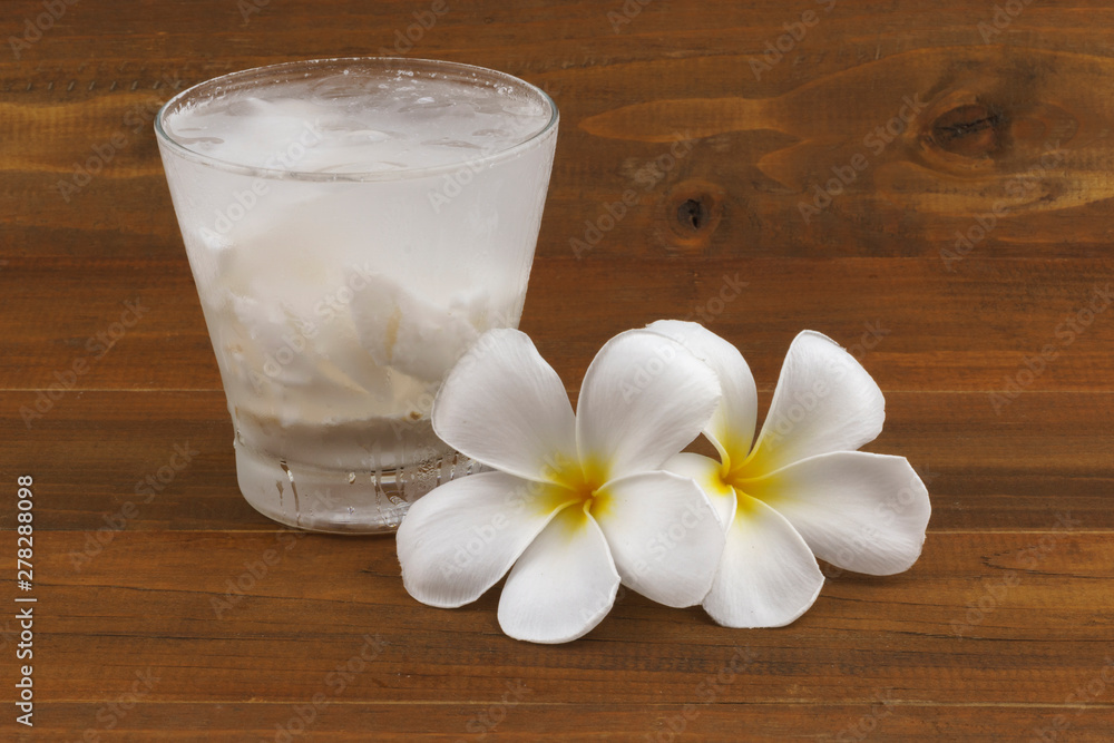 Fresh coconut juice in glass and flower on wooden background Fresh coconut juice in glass and flower on wooden background