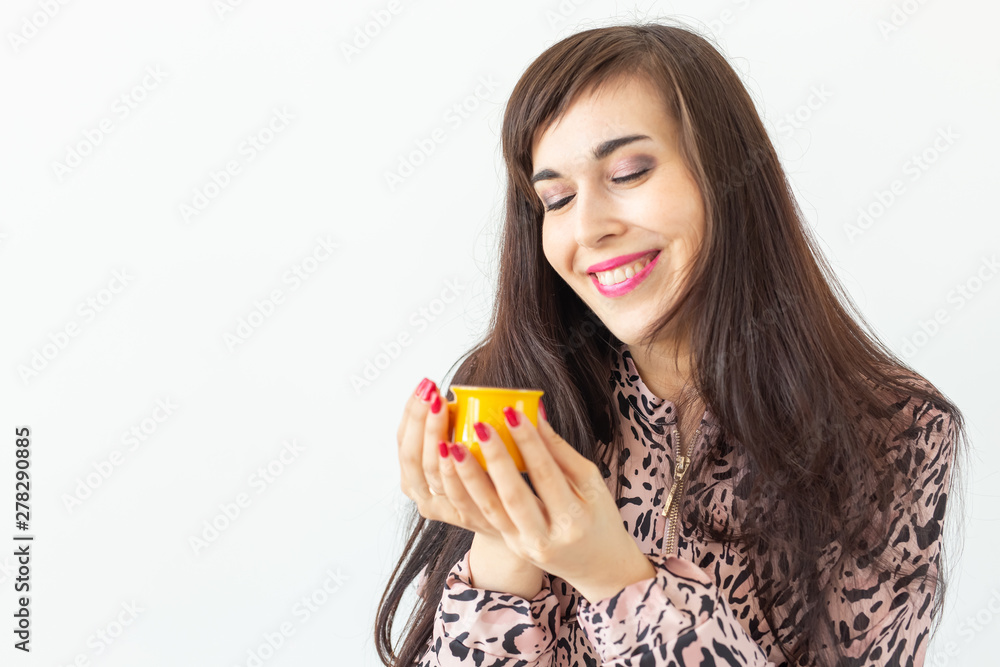 Playful young brunette woman holding in her hands a small yellow mug posing on a white background with copy space. Concept of morning coffee. Playful young brunette woman holding in her hands a small yellow mug posing on a white background with copy space. Concept of morning coffee.