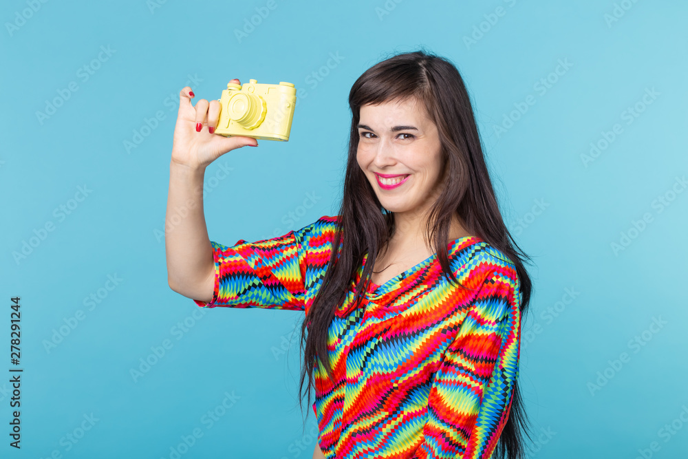 Smiling young woman is holding in her hands a yellow vintage camera model posing on a blue background. Concept of amateur and professional photography. Smiling young woman is holding in her hands a yellow vintage camera model posing on a blue background. Concept of amateur and professional photography.