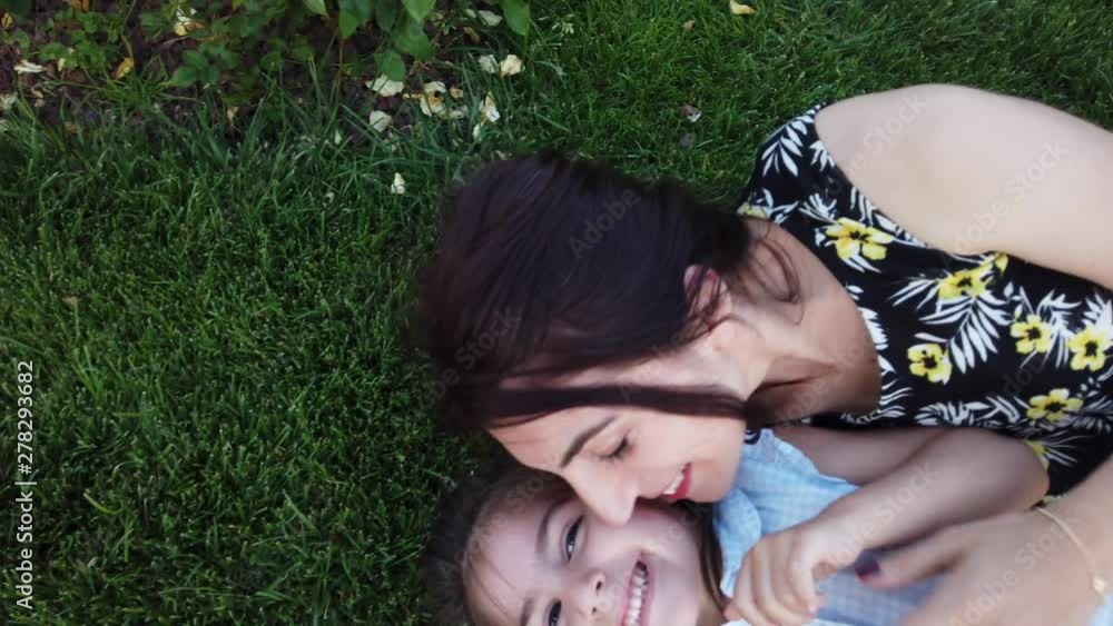 Slow motion:Top view of young mother and her little daughter lying on grass and having fun together Slow motion:Top view of young mother and her little daughter lying on grass and having fun together