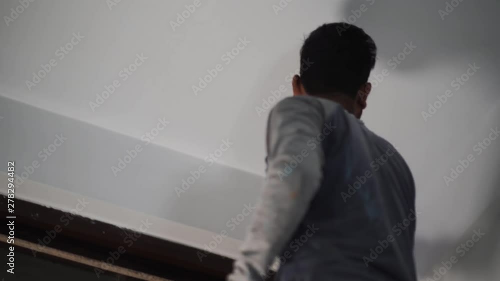 A workman decorating with white paint and a roller A workman decorating with white paint and a roller