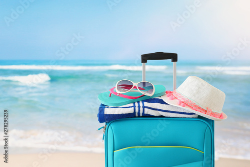 holidays. travel concept. blue suitcase with female hat  flip flips  sunglasses and beach towel in front of tropical background