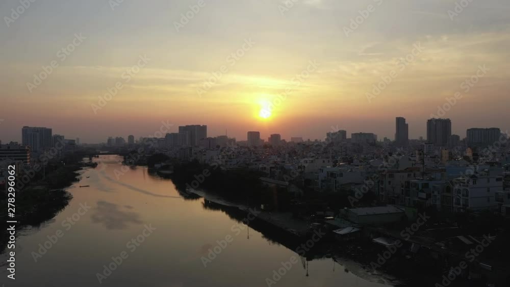 Sunset Drone shot looking along a canal in Ho Chi Minh City (Saigon) Vietnaam over mirror reflection in the water. The high density residential area of district 4 is in silhouette. Sunset Drone shot looking along a canal in Ho Chi Minh City (Saigon) Vietnaam over mirror reflection in the water. The high density residential area of district 4 is in silhouette.