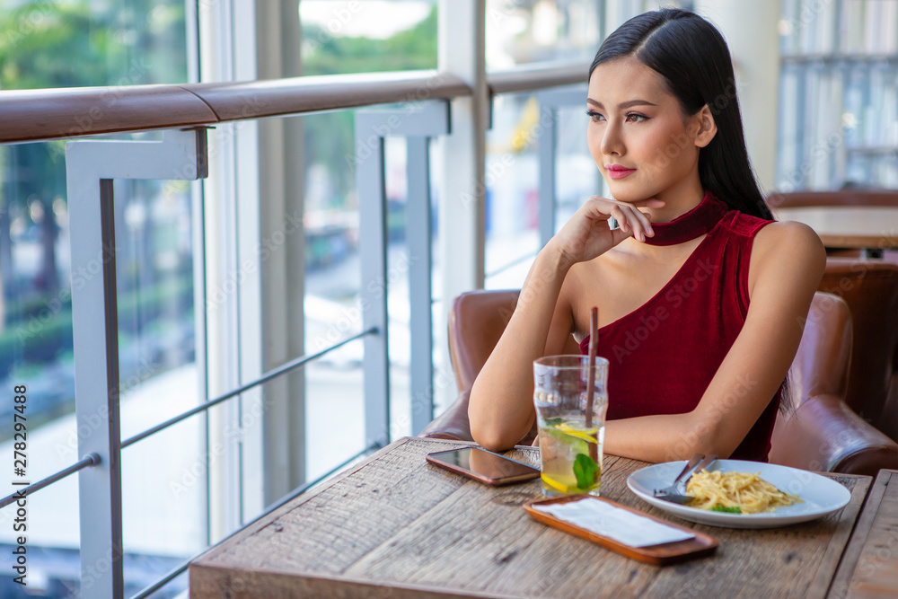 Beautiful young asian woman in red dress sitting in the restaurant looking out the window . happy elegant lady sitting on table thinking and waiting in date Beautiful young asian woman in red dress sitting in the restaurant looking out the window . happy elegant lady sitting on table thinking and waiting in date