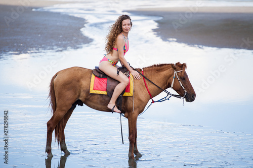 beautiful Young sexy woman wearing bikini  riding a horse  on the sand beach . girl in swimsuit outdoor ,sunny day , summer © iammotos