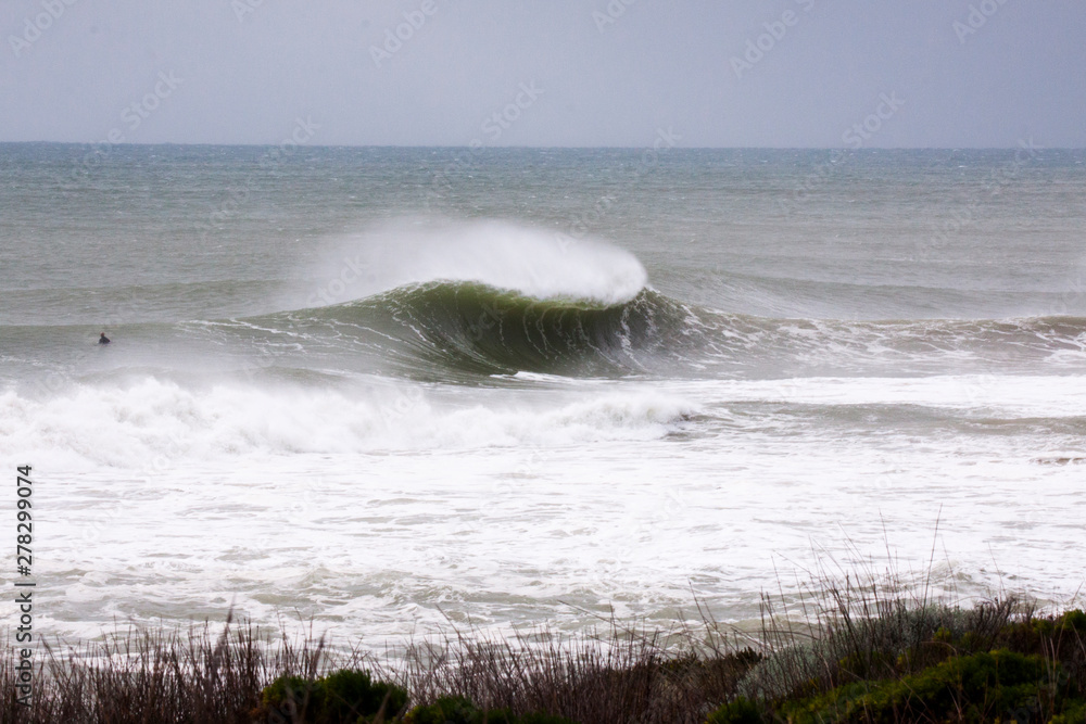 An empty a frame wave breaks and a surfer sits to the side Stock Photo