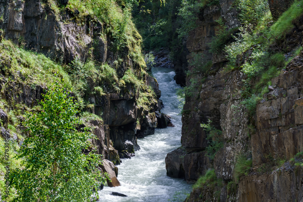 The mountain river flows along the bottom of a deep gorge.