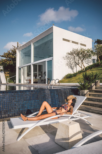 beauty in bikini with cowboy hat relaxing on a sun lounger at a luxury villa