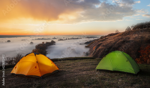 Orange and green tents over river sheltered by mist