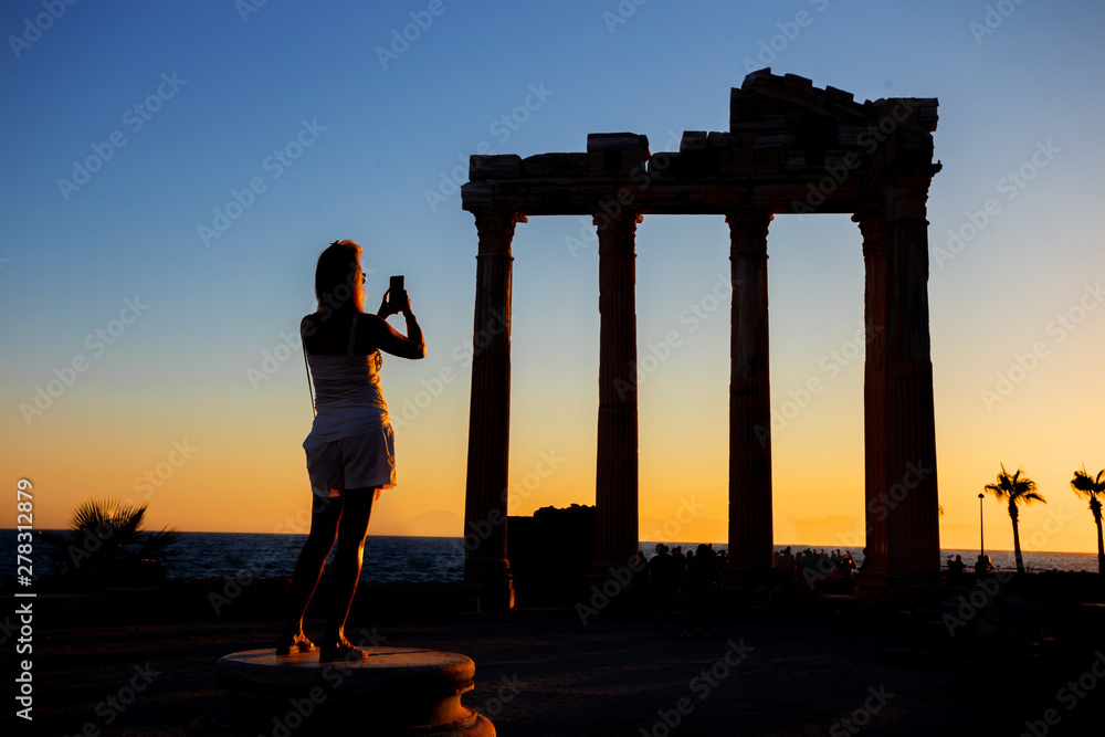 Fototapeta premium Silhouette of girl photographing on phone Temple of Apollo at sunset