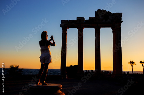 Silhouette of girl photographing on phone Temple of Apollo at sunset