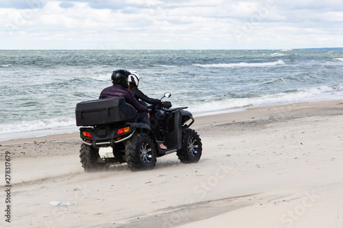 A young guy and a girl in a helmet ride a Quad bike on the beach.