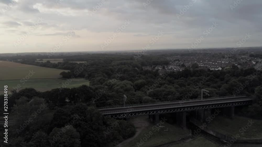 Suburban British village with railway track through middle of scene into distance. Overcast gloomy aerial pull back reveal.