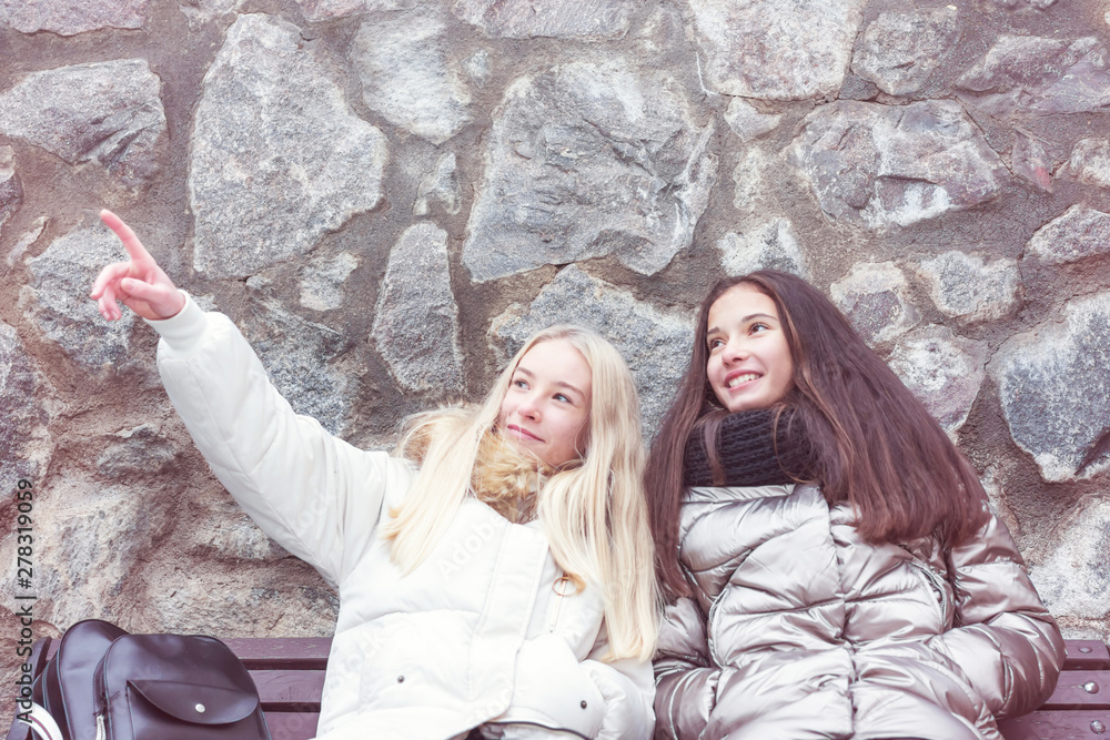 two young girls traveler look at the sights while sitting on a bench, stone wall background, travel and vacation concept two young girls traveler look at the sights while sitting on a bench, stone wall background, travel and vacation concept