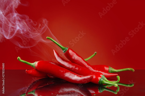 Red hot chillies on red background with reflection and smoke a concept for hot and spicy food