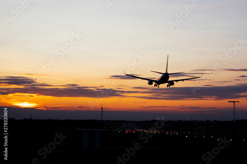 Plane over the landing strip at gold sunset. Cloudy purple sky background.