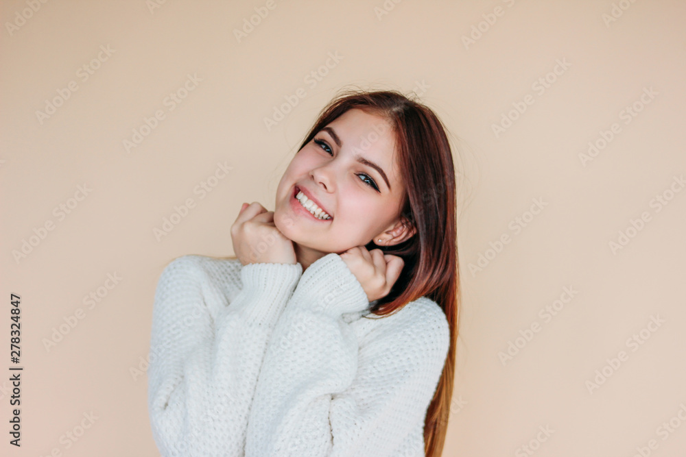Beautiful smiling girl with clean skin and dark long hair in cozy white sweater on beige background Beautiful smiling girl with clean skin and dark long hair in cozy white sweater on beige background
