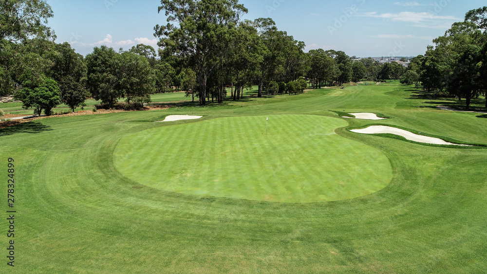 Golf course fairway and green with sand bunker hazards surrounded by trees against blue sky Golf course fairway and green with sand bunker hazards surrounded by trees against blue sky