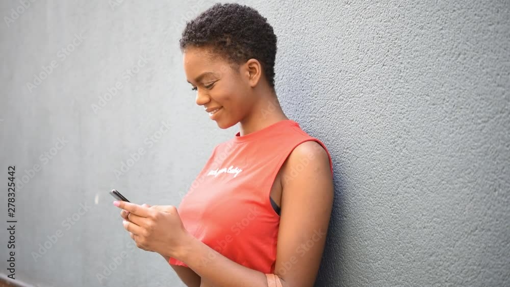 Young black woman texting with her smart phone in urban background. Young black woman texting with her smart phone in urban background.