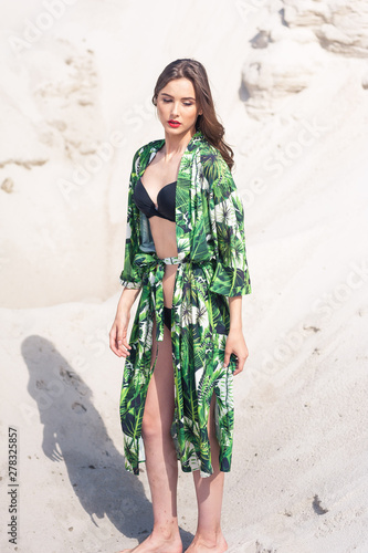 Beautiful young woman walking on the beach, green desert wear.