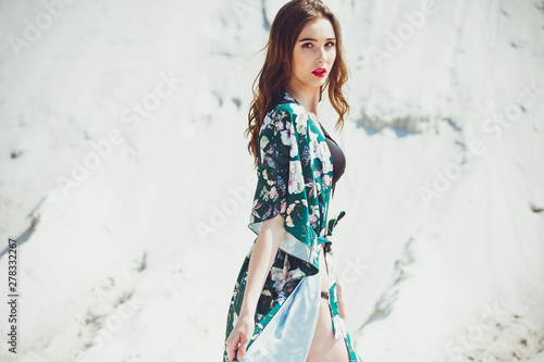 Attractive slender girl in green swimwear posing on white sand beach. Young woman in bikin rests on vacation at sandy ocean shore. Concept travel, swimsuit