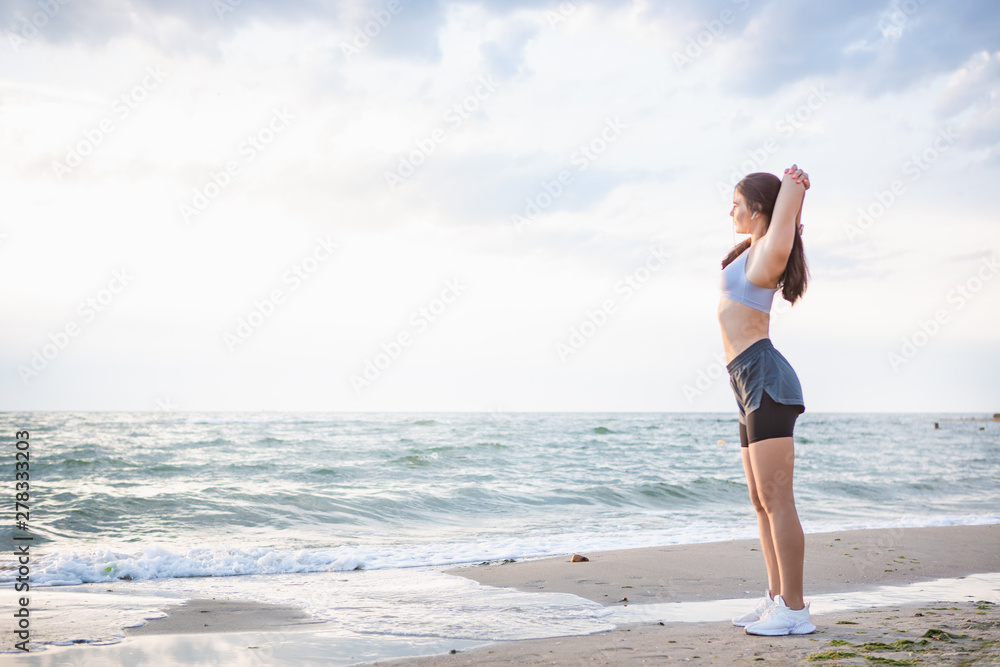 Pretty brunette woman exercising at the sea shore at sunrise listening to the music.
