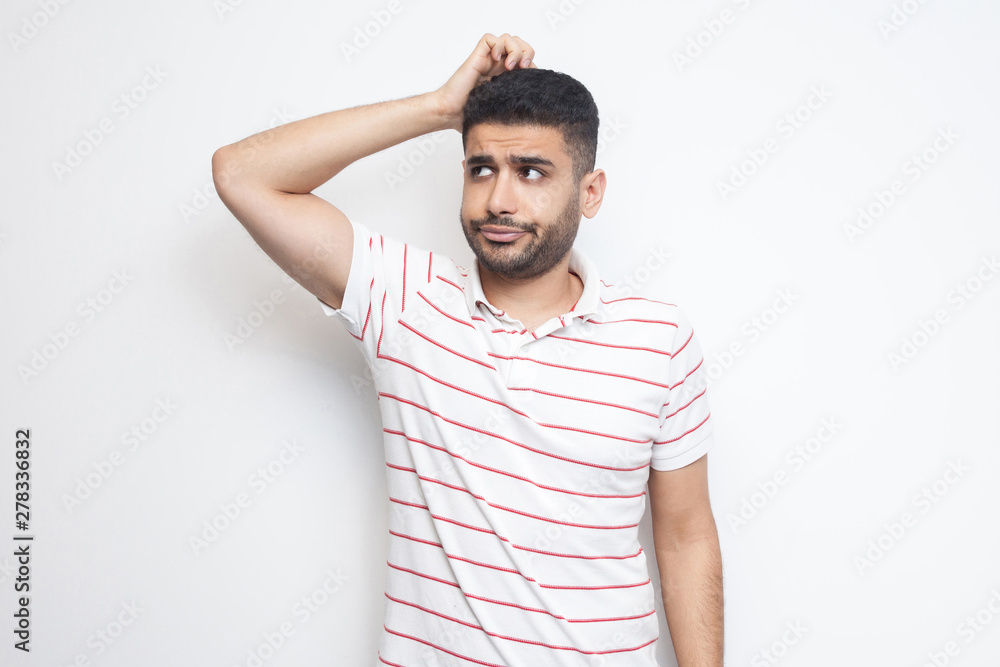 Portrait of query handsome bearded young man in striped t-shirt standing scratching his head, planing and thinking about something. indoor studio shot, isolated on white background. Portrait of query handsome bearded young man in striped t-shirt standing scratching his head, planing and thinking about something. indoor studio shot, isolated on white background.