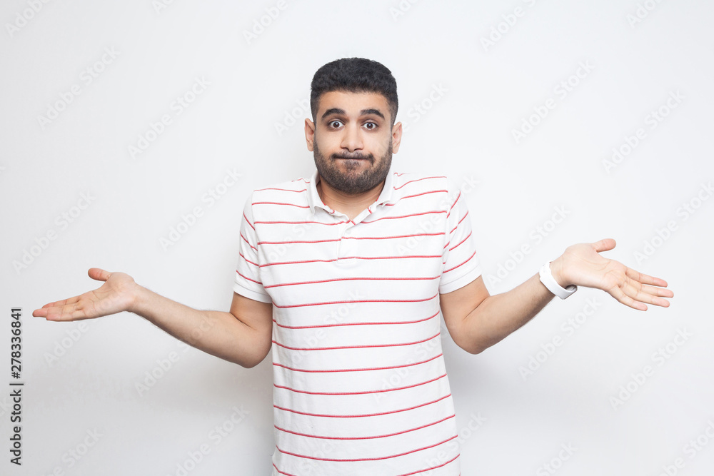 I don't know. Portrait of confused handsome bearded young man in striped t-shirt standing with raised arms and dont know what to do. indoor studio shot, isolated on white background. I don't know. Portrait of confused handsome bearded young man in striped t-shirt standing with raised arms and dont know what to do. indoor studio shot, isolated on white background.