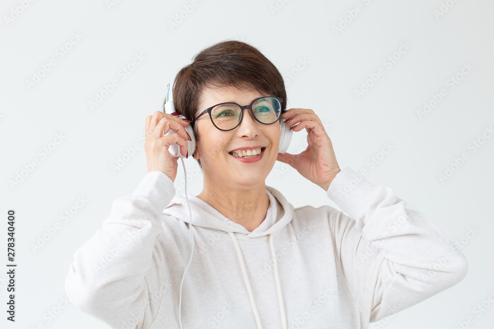 Beautiful middle-aged woman in light sweater and glasses is listening to her favorite music with wire headphones and high-speed Internet. Concept of buying music in online store. Advertising space.