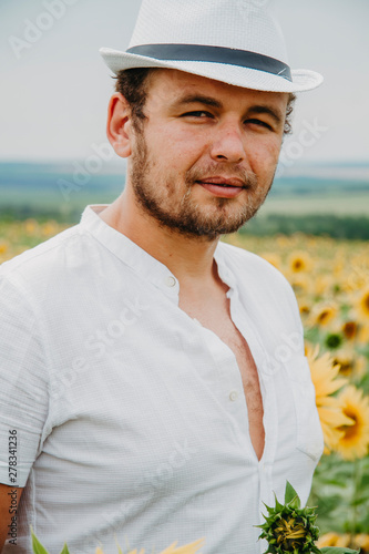 Closeup portrait of a handsome young man in a white shirt and white hat, a serious man with a beard looks into the frame. © Yuliya Timofeeva
